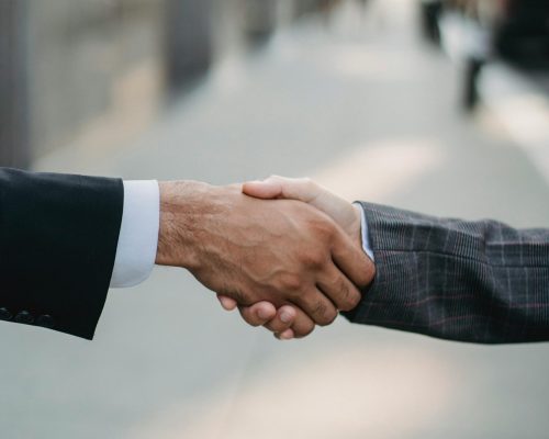 Two businessmen shaking hands outside, symbolizing cooperation and agreement in a city setting.